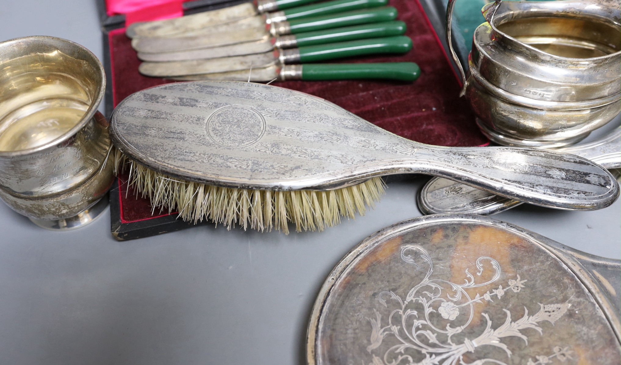 A small group of silver items including a tortoiseshell mounted hand mirror, London, 1917, two silver mounted clothes brushes, a cased set of six teaspoons, a mug and sugar bowl, together with a pair of plated candle snu